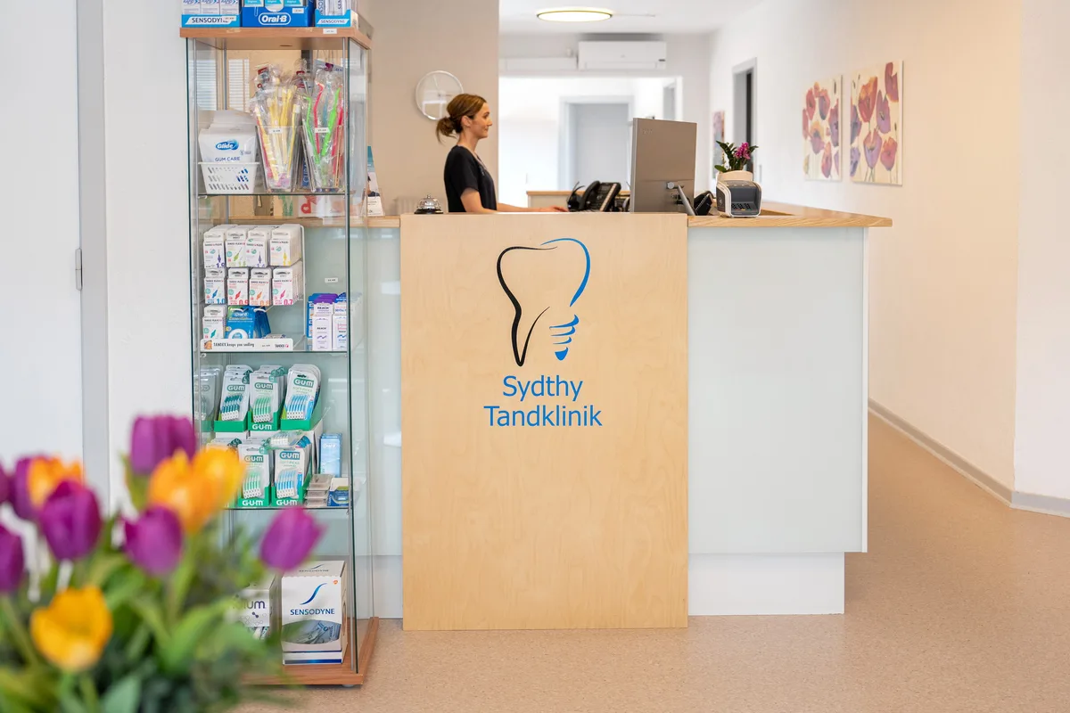 Receptionen hos Sydthy Tandklinik i Hurup - klinikassistent bag skranken med klinikkens logo og gangen ind til klinikkens rum